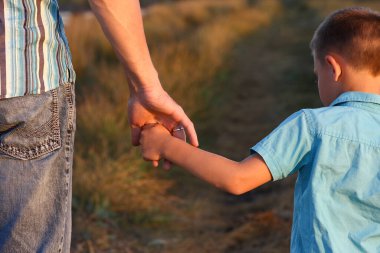 Yolun kenarındaki parkta mutlu bir çocuk ve ebeveynin elleri.