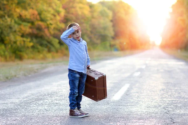 Parktaki yolculukta bavullu yorgun bir çocuk.