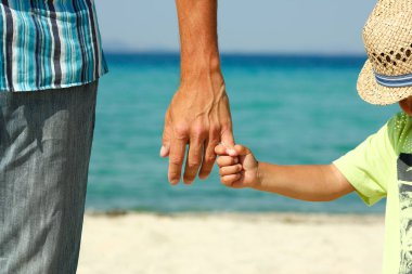 Ebeveyn yazın plajda çocuğun elini tutar.