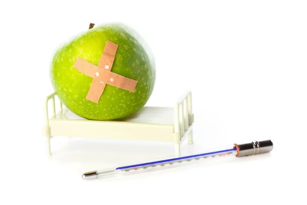 Apple in hospital bed, thermometer in front — Stock Photo, Image