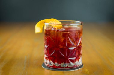 Klasik Negroni Kokteyli. Siyah zemin üzerinde buz ve portakal kabuğu olan retro bardakta. Metin için yer var.