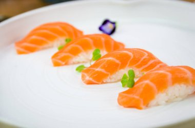 Lezzetli kaliteli somon nigiri, yenilebilir çiçekle süslenmiş el yapımı beyaz tabak..