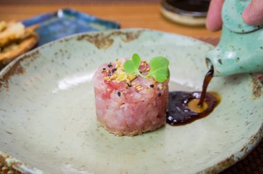 Süslü bir tabakta ton balıklı tartar lezzetine soya sosu döken adam..