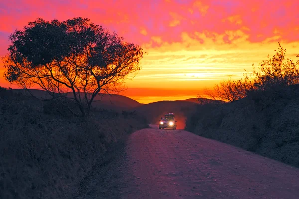 Carro dirigindo em uma estrada de terra com um pôr do sol incrível no oeste — Fotografia de Stock