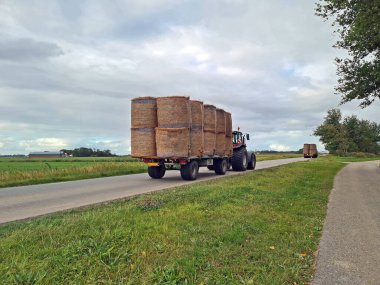 Hollanda, Friesland yolunda hasat edilmiş saman balyalarıyla traktörler.