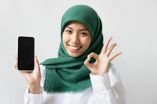 幸せな笑顔のイスラム教徒の女性は黒のスマートフォンの画面にOkの手のサインを与える — ストック写真