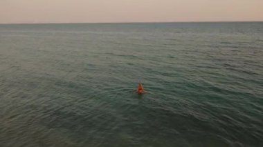Açık deniz günbatımının 4K görüntüsü. Genç bir kadın su okyanusundaki bikini şnorkelli dalış maskesiyle geliyor.. 