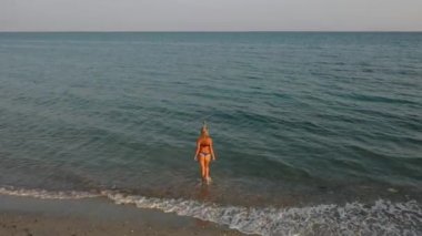 Açık deniz günbatımının üzerindeki 4k hava görüntüsü. Genç bir kadın okyanus mayo bikinisi ile geliyor.
