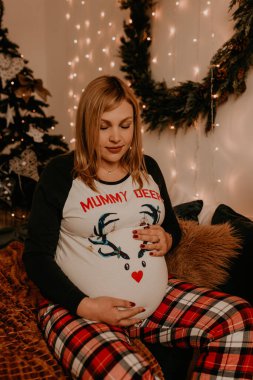 Hamile kadın pijamalarıyla yatak odasında yatağında oturuyor. Noel sabahı. Yılbaşı arifesi. Sevgililer Günü kutlaması