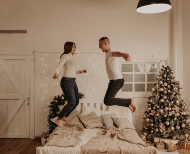 Genç bir çift, yeni yıl için yatak odasındaki ağaçlı evde yatağa atlıyor. Noel sabahı. Dairenin içi. Sevgililer Günü kutlaması