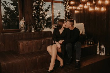 Aşık bir çift, Noel ağacının yanında, tahta bir pencere kenarında öpüşüyorlar. Yeni yıl için dekore edilmiş bir ev. Noel sabahı. Dairenin içi. Sevgililer Günü kutlaması