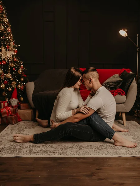 Aşık bir çift yerde bağdaş kurmuş, kucaklaşıyor ve Noel ağacını öpüyor. Yeni yıl için dekore edilmiş bir ev. Noel sabahı. Dairenin içi. Sevgililer Günü kutlaması