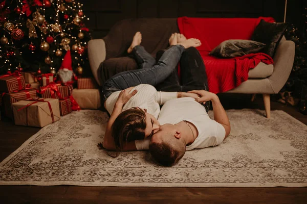 Genç bir çift kanepenin yanında uzanmış ayaklarını uzatmış ve Noel ağacının yanındaki yatak odasında öpüşüyorlar. Yeni yıl için dekore edilmiş bir ev. Sevgililer Günü kutlaması