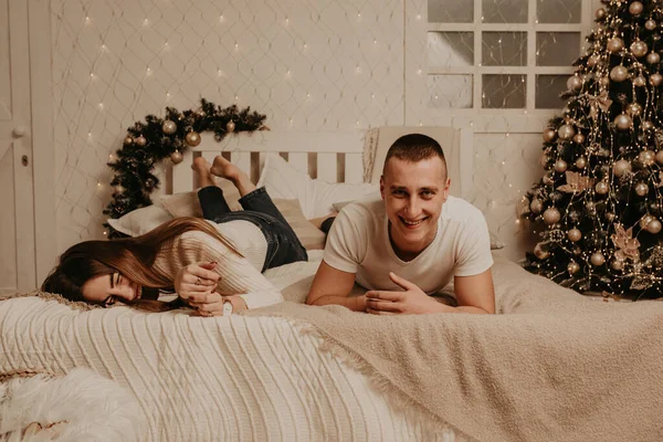 Pár muž a žena ležet na posteli ložnice v blízkosti vánoční strom. — Stock fotografie