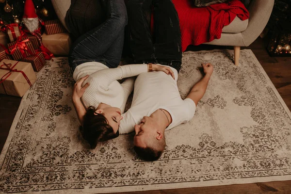 Pár ležet na podlaze u gauče s nohama nahoru líbání v ložnici v blízkosti vánočního stromku — Stock fotografie