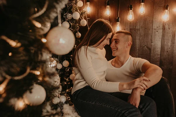 Mann und Mädchen umarmen sich in der Nähe des Weihnachtsbaums am Fenster auf der Holzfensterbank — Stockfoto