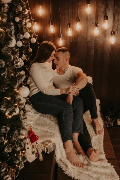 Mann und Mädchen umarmen sich in der Nähe des Weihnachtsbaums am Fenster auf der Holzfensterbank — Stockfoto