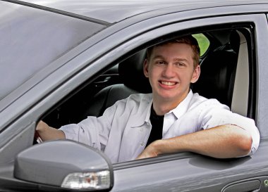 Young man posing next to his gray car for a senior photoshoot.  Auburn red hair.
