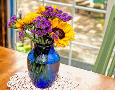 Pretty floral arrangement with sunflowers and purple accent flowers sitting in front of windowpane on table in home