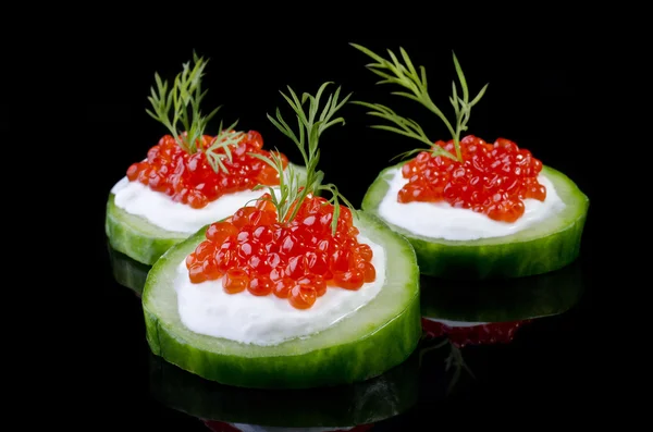 Caviar rojo sobre un pepino verde, aislado sobre negro — Foto de Stock