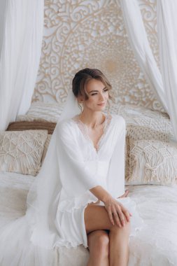 Gelinin kırsal tarzda bir sabah, beyaz bornoz ve beyaz bir buket içinde yatağın ve banyonun yanında bir fotoğraf stüdyosunun, bir otelin penceresinin yanında