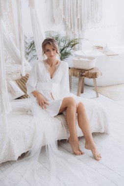 Gelinin kırsal tarzda bir sabah, beyaz bornoz ve beyaz bir buket içinde yatağın ve banyonun yanında bir fotoğraf stüdyosunun, bir otelin penceresinin yanında