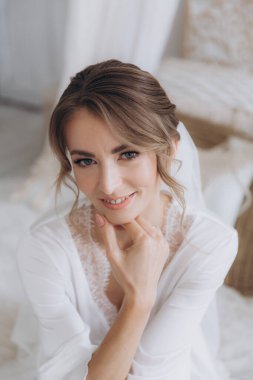 Gelinin kırsal tarzda bir sabah, beyaz bornoz ve beyaz bir buket içinde yatağın ve banyonun yanında bir fotoğraf stüdyosunun, bir otelin penceresinin yanında