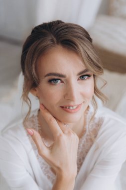 Gelinin kırsal tarzda bir sabah, beyaz bornoz ve beyaz bir buket içinde yatağın ve banyonun yanında bir fotoğraf stüdyosunun, bir otelin penceresinin yanında