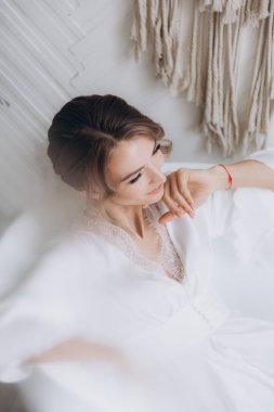 Gelinin kırsal tarzda bir sabah, beyaz bornoz ve beyaz bir buket içinde yatağın ve banyonun yanında bir fotoğraf stüdyosunun, bir otelin penceresinin yanında