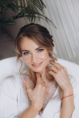 Gelinin kırsal tarzda bir sabah, beyaz bornoz ve beyaz bir buket içinde yatağın ve banyonun yanında bir fotoğraf stüdyosunun, bir otelin penceresinin yanında