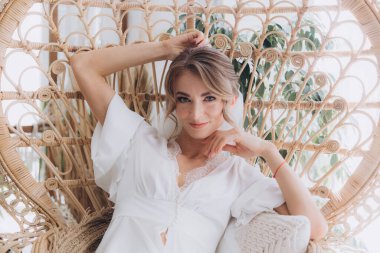 Gelinin kırsal tarzda bir sabah, beyaz bornoz ve beyaz bir buket içinde yatağın ve banyonun yanında bir fotoğraf stüdyosunun, bir otelin penceresinin yanında