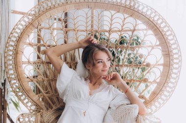 Gelinin kırsal tarzda bir sabah, beyaz bornoz ve beyaz bir buket içinde yatağın ve banyonun yanında bir fotoğraf stüdyosunun, bir otelin penceresinin yanında