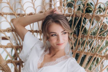 Gelinin kırsal tarzda bir sabah, beyaz bornoz ve beyaz bir buket içinde yatağın ve banyonun yanında bir fotoğraf stüdyosunun, bir otelin penceresinin yanında