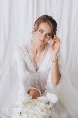 Gelinin kırsal tarzda bir sabah, beyaz bornoz ve beyaz bir buket içinde yatağın ve banyonun yanında bir fotoğraf stüdyosunun, bir otelin penceresinin yanında