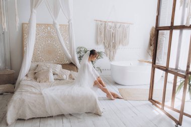Gelinin kırsal tarzda bir sabah, beyaz bornoz ve beyaz bir buket içinde yatağın ve banyonun yanında bir fotoğraf stüdyosunun, bir otelin penceresinin yanında