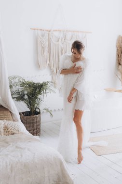 Gelinin kırsal tarzda bir sabah, beyaz bornoz ve beyaz bir buket içinde yatağın ve banyonun yanında bir fotoğraf stüdyosunun, bir otelin penceresinin yanında