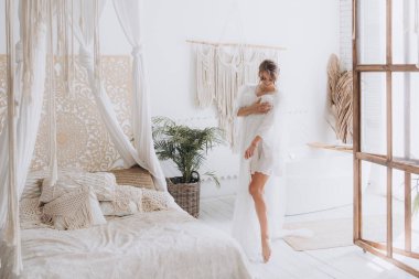 Gelinin kırsal tarzda bir sabah, beyaz bornoz ve beyaz bir buket içinde yatağın ve banyonun yanında bir fotoğraf stüdyosunun, bir otelin penceresinin yanında