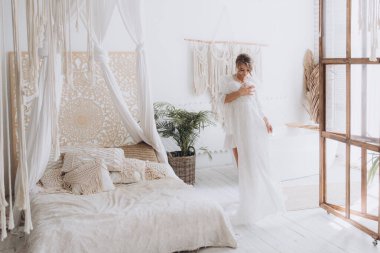 Gelinin kırsal tarzda bir sabah, beyaz bornoz ve beyaz bir buket içinde yatağın ve banyonun yanında bir fotoğraf stüdyosunun, bir otelin penceresinin yanında