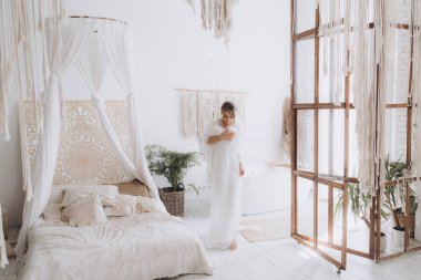 Gelinin kırsal tarzda bir sabah, beyaz bornoz ve beyaz bir buket içinde yatağın ve banyonun yanında bir fotoğraf stüdyosunun, bir otelin penceresinin yanında