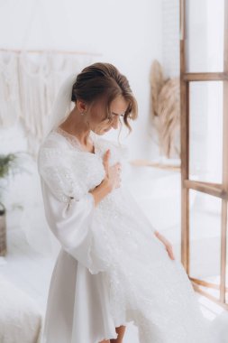 Gelinin kırsal tarzda bir sabah, beyaz bornoz ve beyaz bir buket içinde yatağın ve banyonun yanında bir fotoğraf stüdyosunun, bir otelin penceresinin yanında