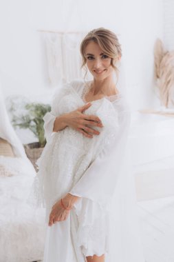 Gelinin kırsal tarzda bir sabah, beyaz bornoz ve beyaz bir buket içinde yatağın ve banyonun yanında bir fotoğraf stüdyosunun, bir otelin penceresinin yanında