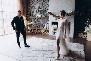 Siyah takım elbiseli damadın ilk buluşması ve siyah arka planda bir fotoğraf stüdyosunun, otelin içinde beyaz gelinlik içinde bir buket.