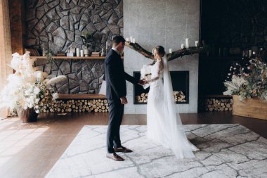 Siyah takım elbiseli damadın ilk buluşması ve siyah arka planda bir fotoğraf stüdyosunun, otelin içinde beyaz gelinlik içinde bir buket.