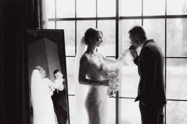 Siyah takım elbiseli damadın ilk buluşması ve siyah arka planda bir fotoğraf stüdyosunun, otelin içinde beyaz gelinlik içinde bir buket.