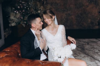 Siyah takım elbiseli damadın ilk buluşması ve siyah arka planda bir fotoğraf stüdyosunun, otelin içinde beyaz gelinlik içinde bir buket.