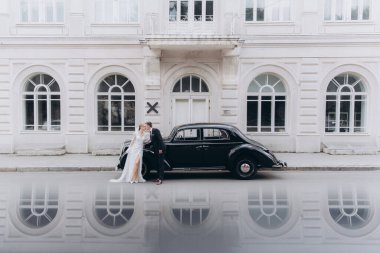 Güzel, şık bir çiftin düğünü, beyaz gelinlikli bir gelin ve siyah takım elbiseli bir damat, smokin, siyah bir retro araba..