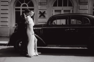 Güzel, şık bir çiftin düğünü, beyaz gelinlikli bir gelin ve siyah takım elbiseli bir damat, smokin, siyah bir retro araba..
