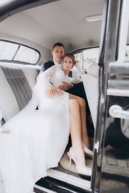 Güzel, şık bir çiftin düğünü, beyaz gelinlikli bir gelin ve siyah takım elbiseli bir damat, smokin, siyah bir retro araba..