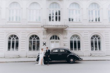 Güzel, şık bir çiftin düğünü, beyaz gelinlikli bir gelin ve siyah takım elbiseli bir damat, smokin, siyah bir retro araba..