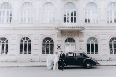 Güzel, şık bir çiftin düğünü, beyaz gelinlikli bir gelin ve siyah takım elbiseli bir damat, smokin, siyah bir retro araba..